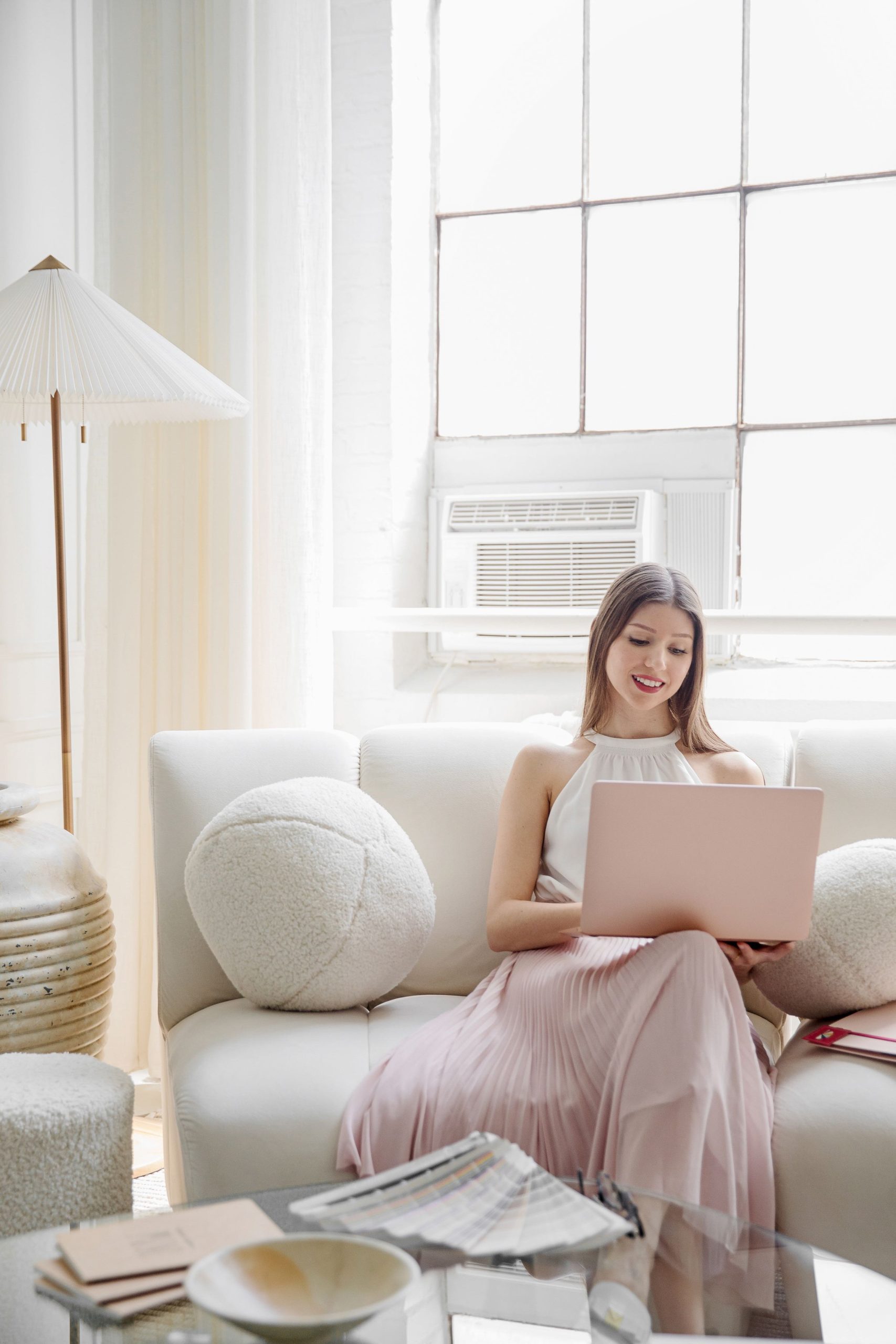 woman sitting on couch in white top and pink skirt with laptop open
